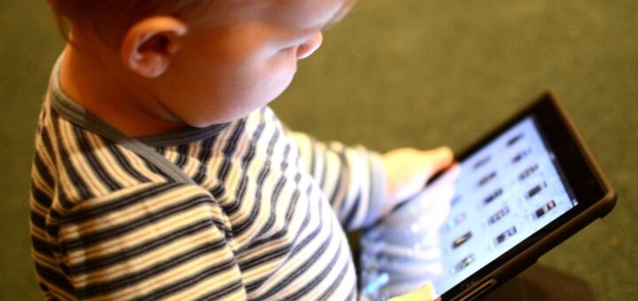 dziecko przedszkolne siedzi na podłodze z tabletem w rękach, skupione na ekranie