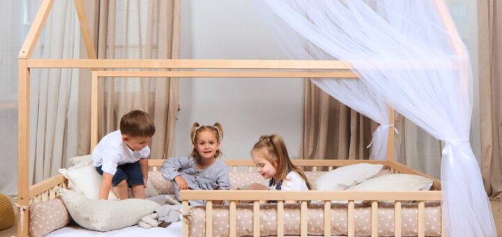 Jasny pokój dziecka z niskim łóżkiem regałami z zabawkami i bawiącym się maluchem